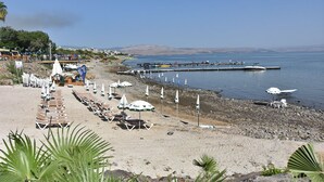 A beach with rows of sun loungers and umbrellas, a pier extending into the water, and a clear view of the distant hills. - The Kings Towers (Tiberias)