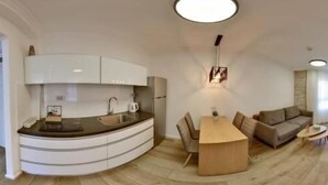 A modern kitchen with a built-in island, a dining area with a wooden table and chairs, a sofa, and a small side table.