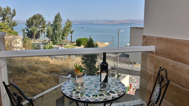 A balcony with a table, a bottle of wine, and a glass. The view includes a body of water and distant hills.