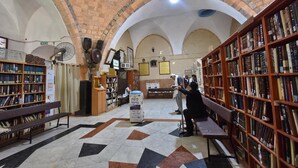 A library with arched ceilings, bookshelves, and a central area with a bench and a fan.