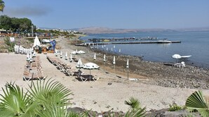 A beach with rows of sun loungers and umbrellas, a rocky shoreline, and a pier extending into the water.