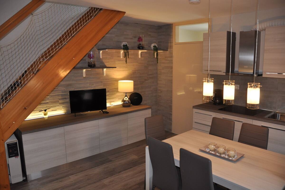 A modern kitchen with a built-in stove, a dining area with a table and chairs, and a staircase with a wooden railing.