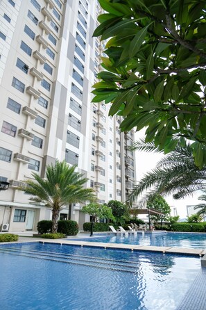 A swimming pool with clear blue water, surrounded by lush greenery and a tall residential building in the background. - Studio Condo at Horizons 101 (Cebu City)