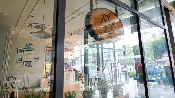 Ein modernes Interieur mit einem großen Glasfenster, einem sichtbaren Logo und einer Sitzecke mit Stühlen und Tischen.