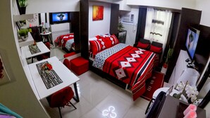 Ein kleines Hotelzimmer mit Bett, Schreibtisch, Stuhl, Fernseher und Nachttisch.