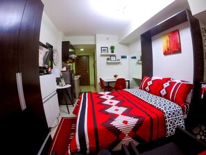 A compact hotel room with a bed, a desk, and a kitchenette. - Studio Condo at Horizons 101 (Cebu City)