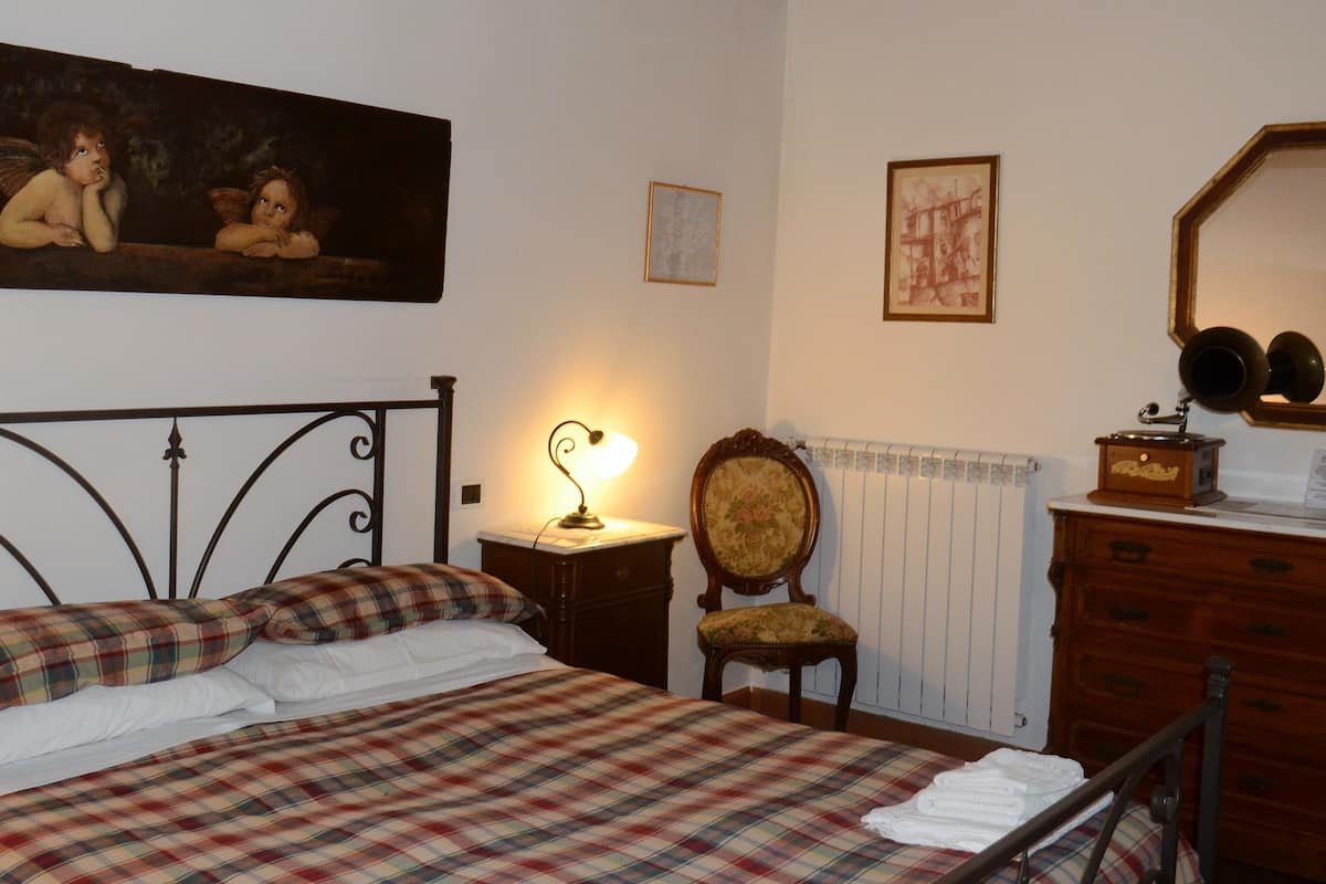 Ein Schlafzimmer mit Bett, Sessel, Schminktisch und Heizkörper. An der Wand hängt ein Bild.