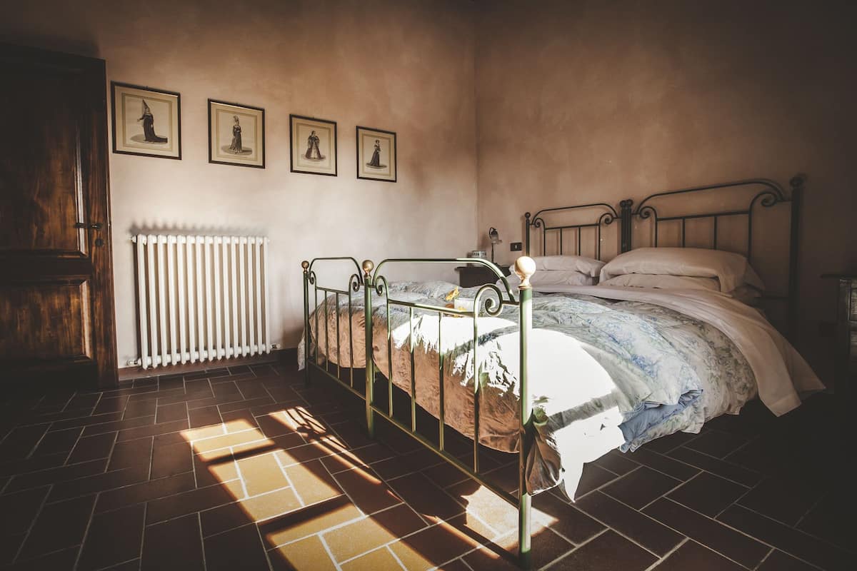 Ein Schlafzimmer mit einem Metallbettgestell, einem Heizkörper und drei gerahmten Bildern an der Wand.