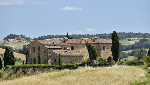 A stone building with a tiled roof, surrounded by dry grass and trees, set in a hilly landscape. - Zampugna (Trequanda)