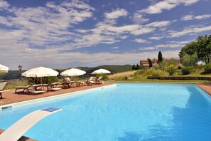 A swimming pool with lounge chairs and umbrellas, surrounded by greenery and a clear sky. - Zampugna (Trequanda)