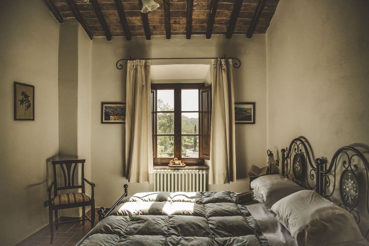 Ein Schlafzimmer mit Bett, einem Sessel, einem Fenster mit Vorhängen und einer Heizung.