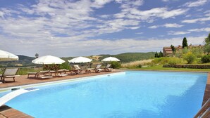 A swimming pool with lounge chairs and umbrellas, surrounded by greenery and hills. - Zampugna (Trequanda)