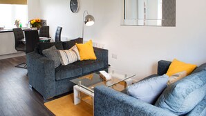 Un salon moderne avec un canapé gris, une table basse et un coin repas comprenant des chaises et une table.