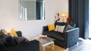 Un salon moderne avec un canapé gris, une table basse en verre et un grand miroir au mur.