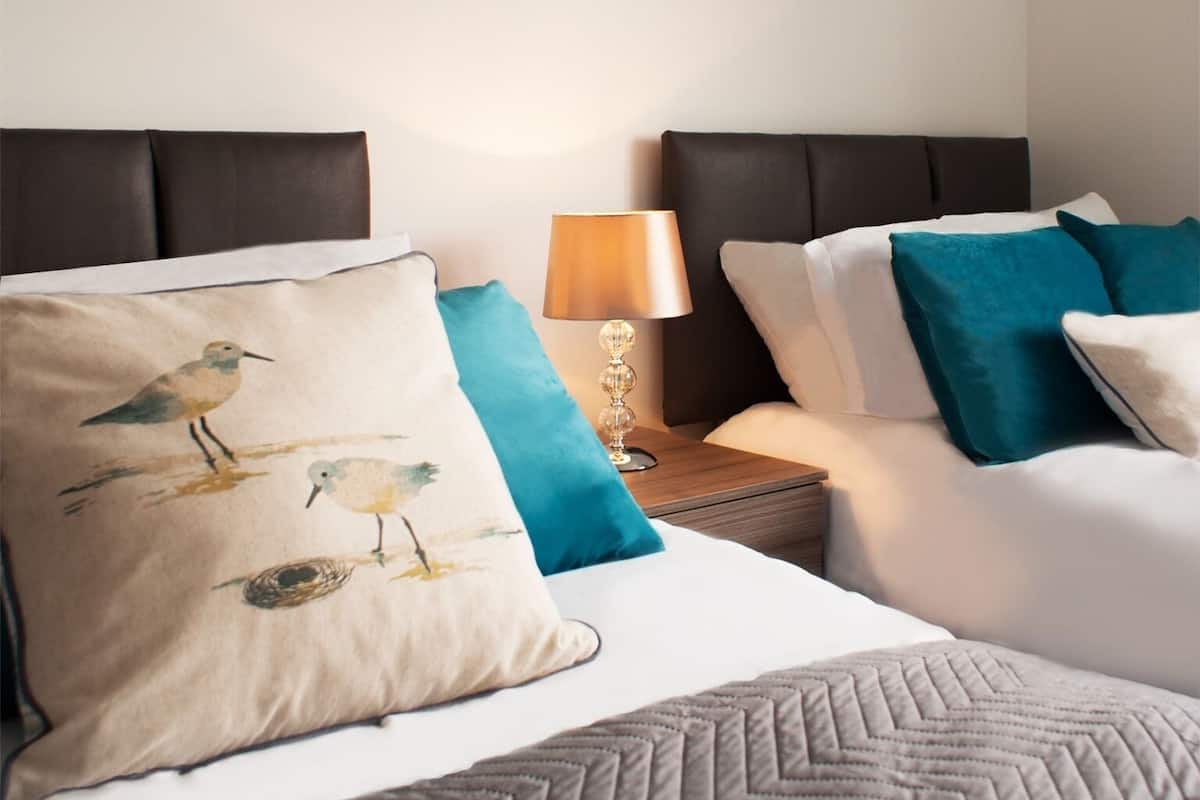 A hotel room with a bed, two nightstands, a lamp, and decorative pillows.