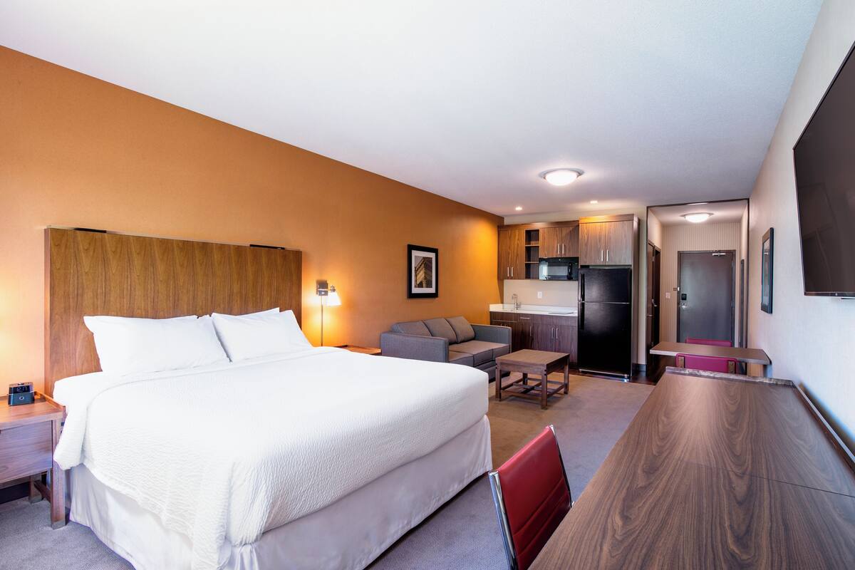 Ein Hotelzimmer mit einem großen Bett, einem Schreibtisch, einer Sitzecke und einer Küchenzeile.