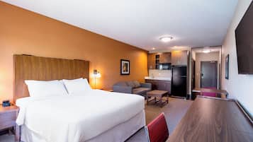 A hotel room with a large bed, a desk, a sofa, and a kitchenette.