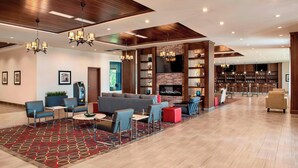 Un hall d’entrée spacieux au design moderne, comprenant un coin salon avec des canapés et des fauteuils, une cheminée et un bar avec des étagères et un téléviseur.