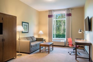 A furnished room with a sofa, a desk, a chair, a lamp, a picture on the wall, and a window with curtains. - Four Points by Sheraton Grande Prairie (Grande Prairie)
