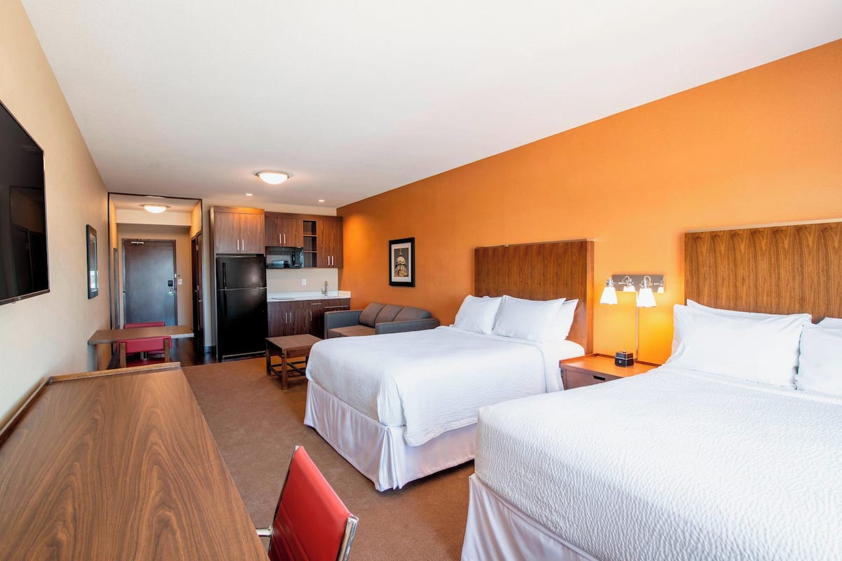Ein Hotelzimmer mit zwei Betten, einem Schreibtisch, einem Stuhl, einer Küchenzeile und einem Badezimmer.