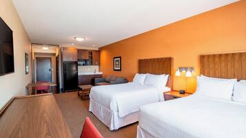 Habitación de hotel con dos camas, un escritorio, una silla, una kitchenette y un baño.