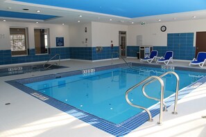 A swimming pool with blue tiled walls and a metal ladder. There are lounge chairs and a door with a sign. - Four Points by Sheraton Grande Prairie (Grande Prairie)