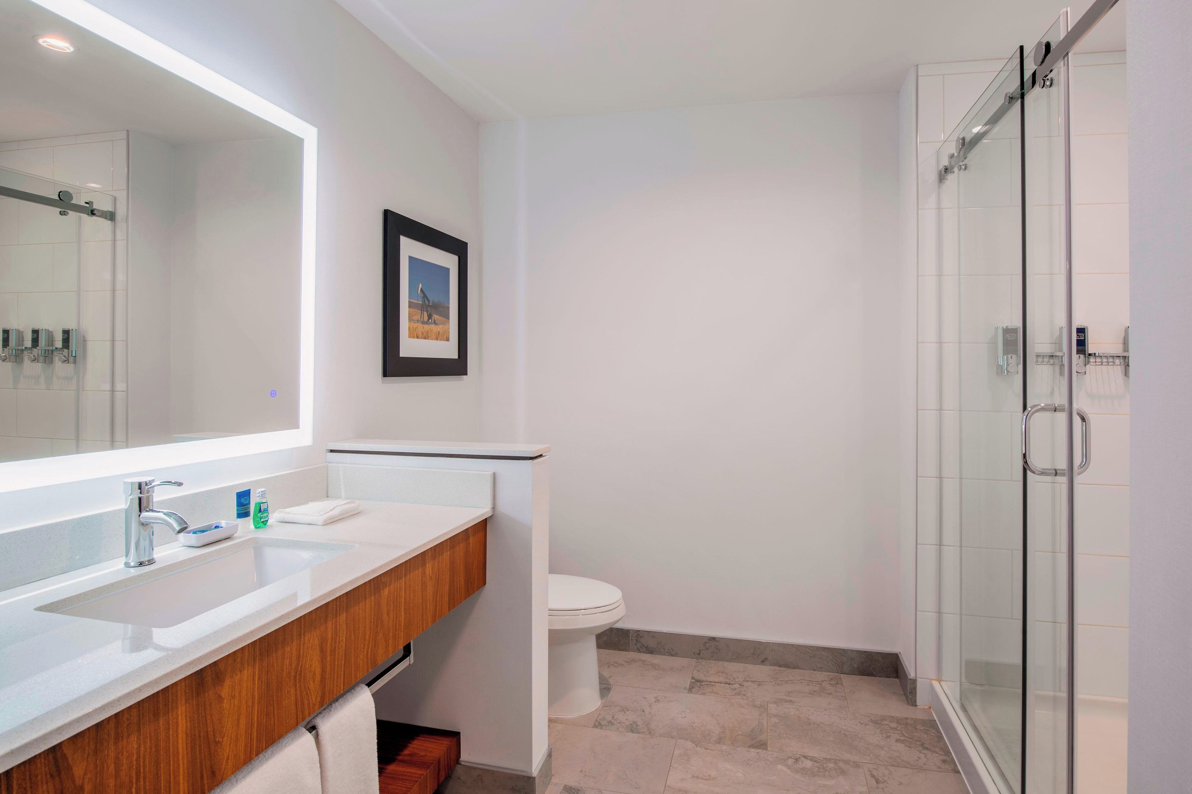 A modern bathroom with a large mirror, a wooden vanity, a toilet, and a glass shower enclosure.