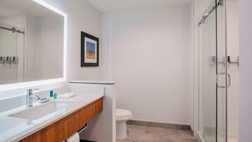 A modern bathroom with a large mirror, a wooden vanity, a toilet, and a glass shower enclosure.