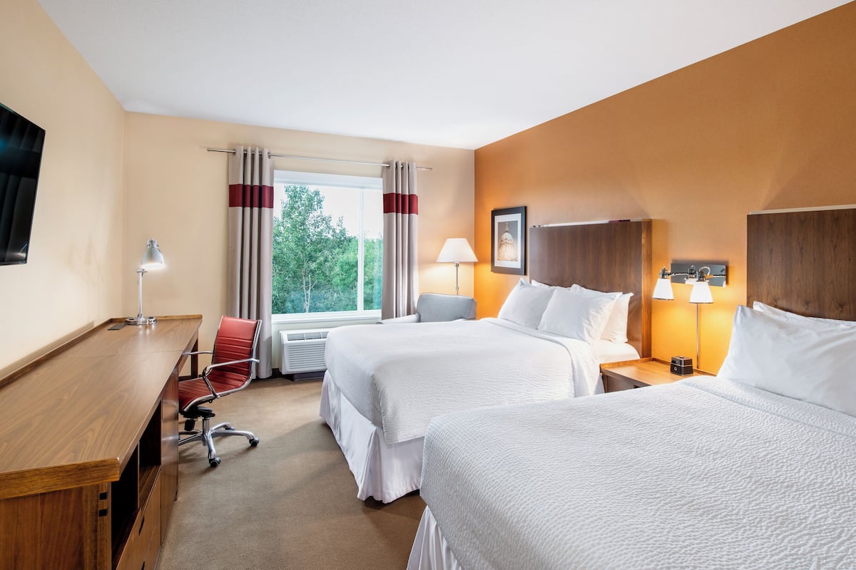 Ein Hotelzimmer mit zwei Betten, einem Schreibtisch, einem Stuhl, einer Lampe und einem fenster mit Vorhängen.