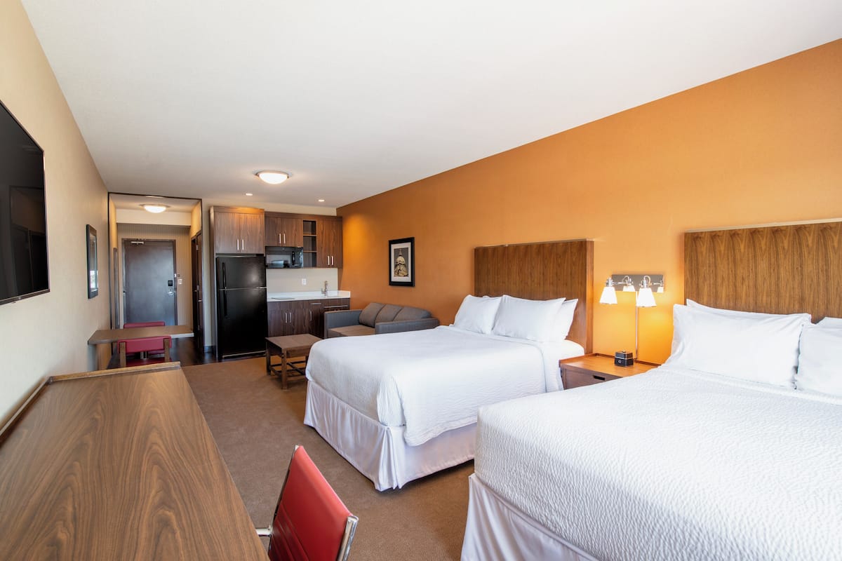 Ein Hotelzimmer mit zwei Betten, einem Schreibtisch, einer Küchenzeile und einem Fernseher.