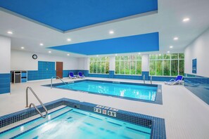 Une piscine intérieure à l’eau claire, avec des murs recouverts de carreaux bleus et une horloge au mur.