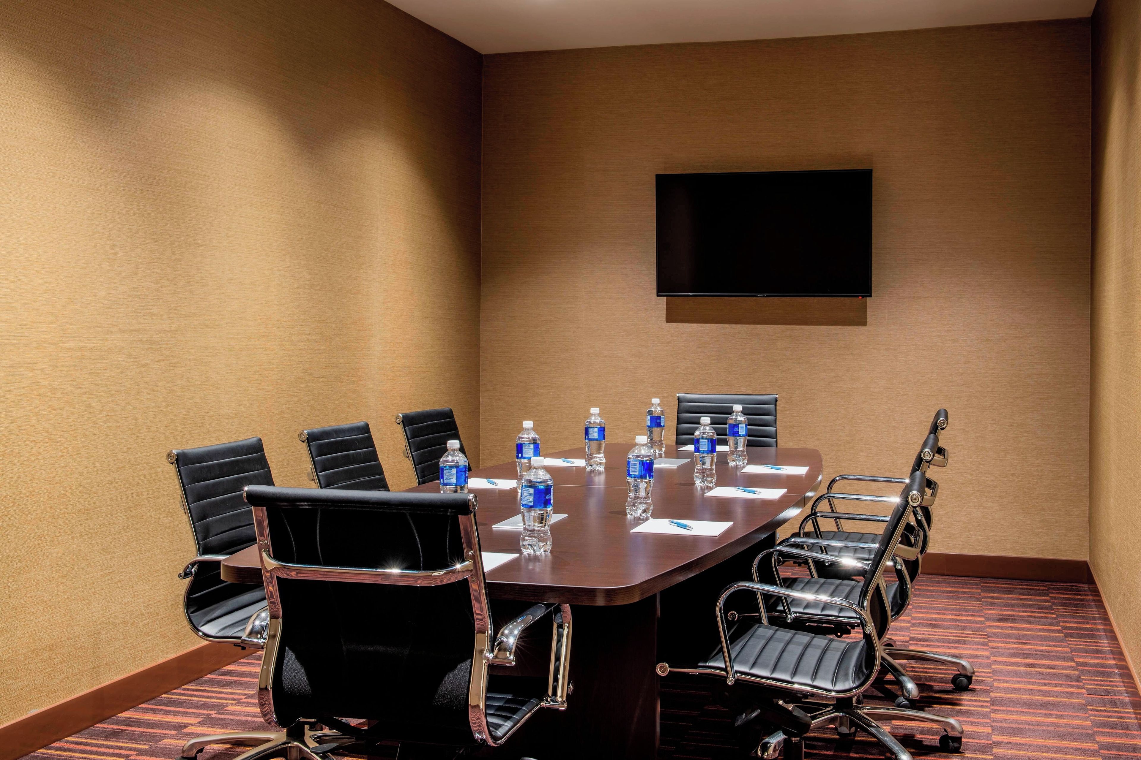 A conference room with a large table, chairs, water bottles, and a flat-screen TV on the wall.