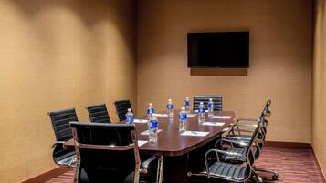 A conference room with a large table, chairs, water bottles, and a flat-screen TV on the wall.