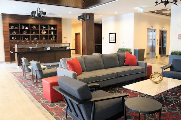A modern lobby with a sofa, chairs, a coffee table, and a reception desk. - Four Points by Sheraton Grande Prairie (Grande Prairie)