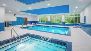 Une piscine intérieure aux carreaux bleu clair, une horloge au mur et une porte.