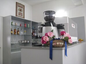 Una cocina con cafetera, repisas con botellas y una cesta decorativa con flores.