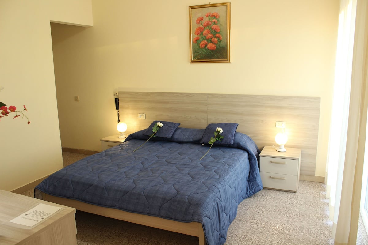 A neatly arranged bedroom with a large bed, two bedside tables with lamps, a nightstand, and a painting on the wall.