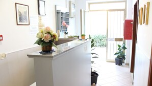 A reception area with a white counter, a vase of flowers, and potted plants. - Hotel Luca (Camaiore)