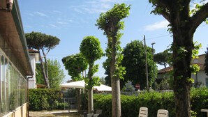 A patio area with outdoor seating, a white umbrella, and a gravel path. - Hotel Luca (Camaiore)
