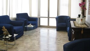 A room with two blue armchairs, a small table with a decorative item, and a vase with flowers on a side table. - Hotel Luca (Camaiore)