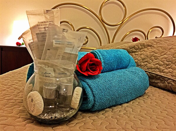 Ein Bett mit blauem Handtuch und einer Rose, ein Glasbehälter mit Pflegeprodukten und ein Metall-Kopfstück.