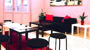 A cozy room with a dining table, chairs, a black sofa with red cushions, a small white table with a plant, and a large window with a view of a rocky stream. - Rho Gloria 2 (Rho)