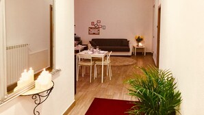 A living room with a dark-colored sofa, a dining table with chairs, a mirror, and a small side table with candles. - Rho Gloria 2 (Rho)