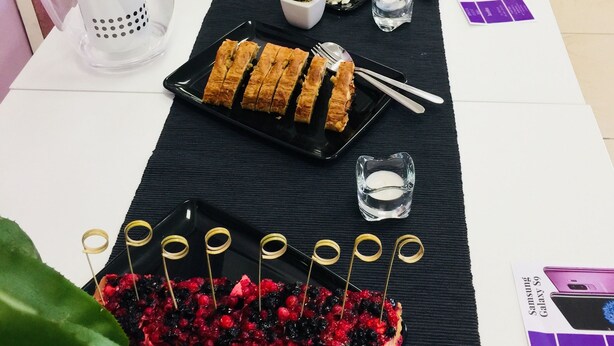 A table set with various food items, including a cake, fruit, and pastries, along with glasses of water and a bottle of champagne. - Rho Gloria 2 (Rho)