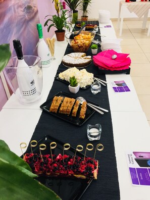 Una mesa dispuesta con diferentes alimentos, como un pastel, fruta y pasteles, junto con vasos de agua y una botella de champán.