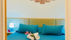 A hotel room with a bed, blue bedding, a headboard, a nightstand with a lamp, and a wall with three framed pictures. - Rho Gloria 2 (Rho)