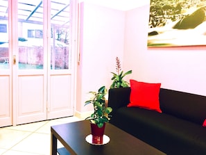 Een woonkamer met een zwarte bank, een rode kussen en een plant in een pot op een tafel.