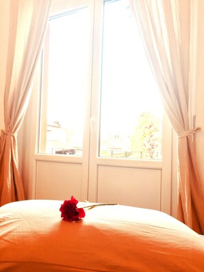 Ein Zimmer mit einem Bett, einem Vorhangfenster und Blick auf Gebäude.
