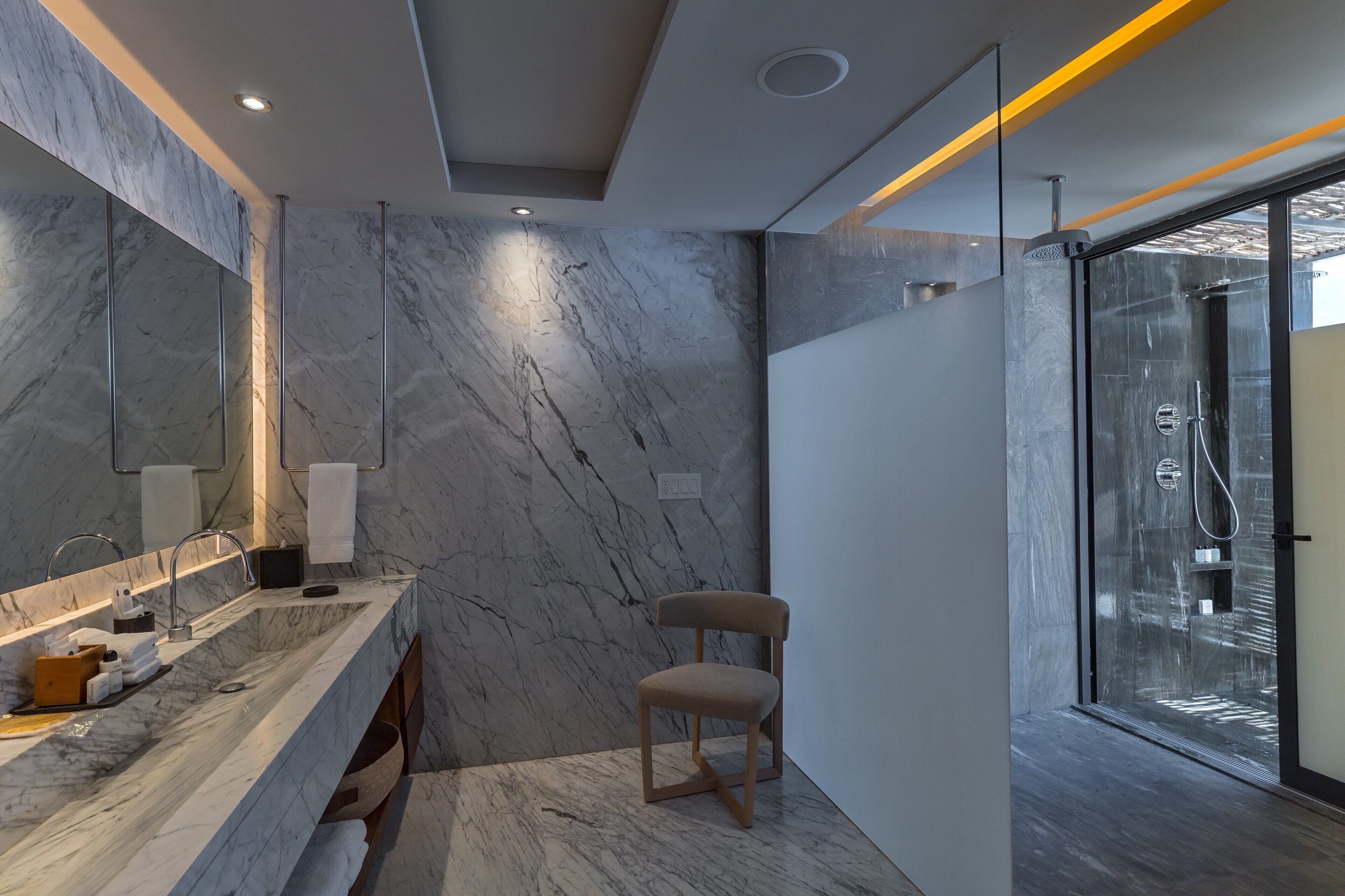 A modern bathroom with a marble vanity, a glass shower enclosure, and a view of the outdoors.