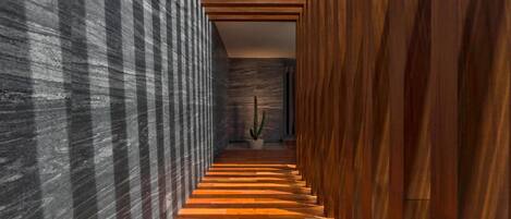 A narrow hallway with wooden flooring and walls, leading to a cactus plant in the distance.